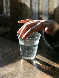 Cropped hand touching drinking glass on wooden table
