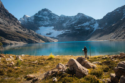 Rear view of man standing on rock by lake against sky