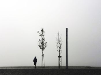 Silhouette man walking on footpath against sky during foggy weather