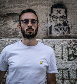 Portrait of young man standing against graffiti wall