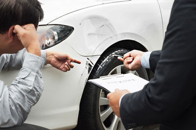 Man showing damaged car to insurance agent with clipboard 