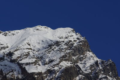 Low angle view of snowcapped mountain against clear blue sky