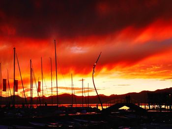 Sailboats moored in sea against dramatic sky during sunset