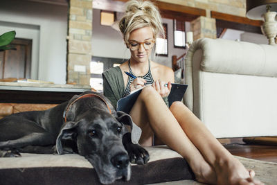 Woman writing diary while sitting by great dane on pet bed at home