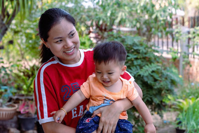 Happy big laughing child boy and young woman holding adorable baby boy outdoors at home. 