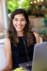 Happy woman working remotely on laptop at outdoor cafe and looking into camera