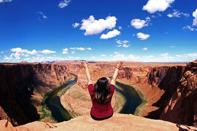 Rear view of woman sitting on rock against sky