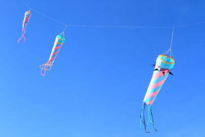 Low angle view of kites flying in clear blue sky