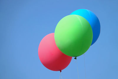 Three colorful balloons fly together in the blue sky