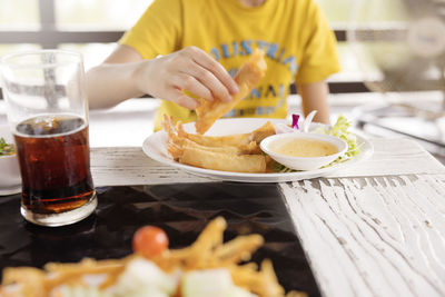 Boy sitting at table and eating spring rolls