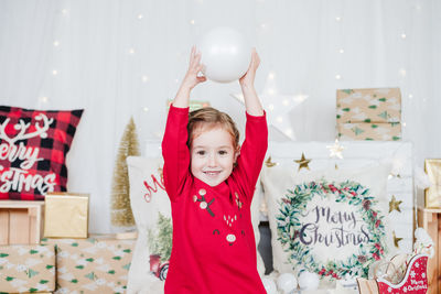 Smiling little girl wearing red christmas dress at home over christmas decoration.