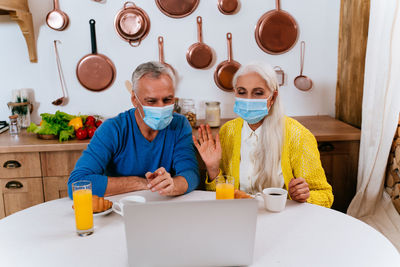 Senior couple wearing mask video calling in laptop at home