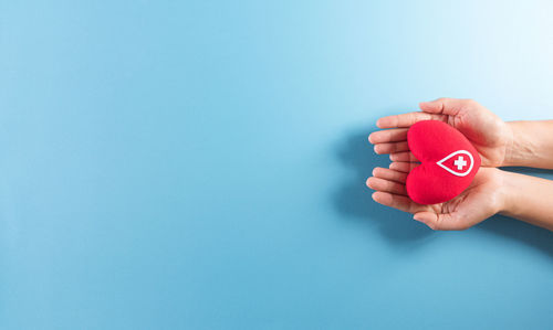 Midsection of woman holding red umbrella against blue background