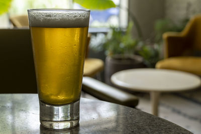 Glass of beer on a terrazzo table, two yellow chairs in the background, retro table, window with 