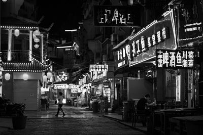 People on illuminated street amidst buildings in city at night