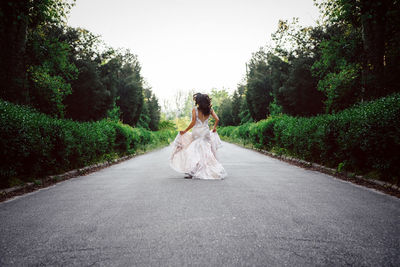 Rear view of woman on road amidst trees against sky