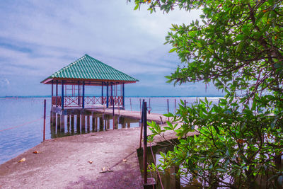 Stilt house by sea against sky