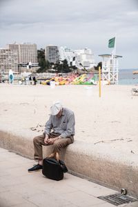 Man sitting on beach in city against sky