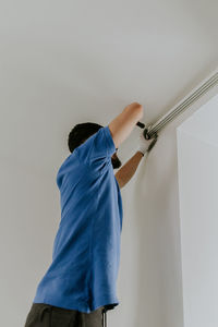A young man unscrews a bolt from a cornice with a screwdriver.
