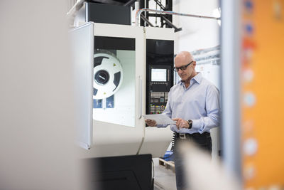 Man with tablet at machine on factory shop floor