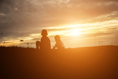 Silhouette people sitting on land against sky during sunset