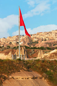 A large red national flag of turkey on metal stele against the background of the village of uchisar.