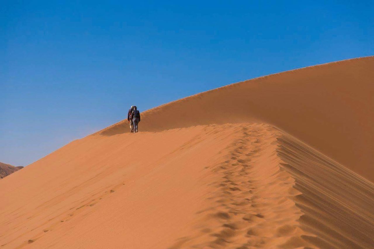 MAN STANDING ON SAND DUNE AGAINST CLEAR BLUE SKY