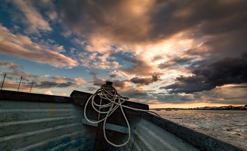 Rope on boat at beach against cloudy sky during sunset