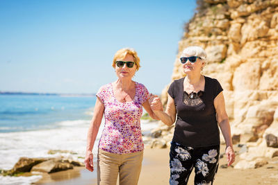 Two elderly women are walking along the rocky shore