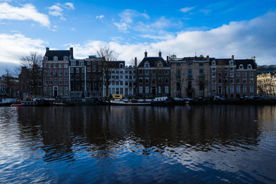 Sailboats moored in river by buildings against sky