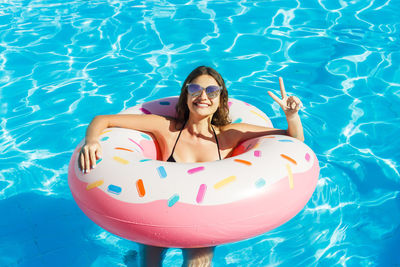 Smiling young woman enjoying in swimming pool with inflatable ring during summer