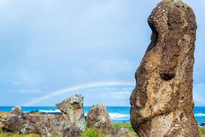 Close-up of moai at easter island with rainbow in background