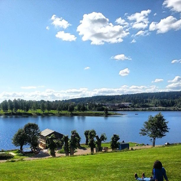 grass, lake, sky, tranquil scene, tranquility, water, scenics, beauty in nature, tree, blue, nature, mountain, leisure activity, cloud - sky, landscape, lifestyles, cloud, lakeshore, field