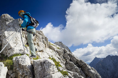 Low angle view of woman climbing on rock formation against sky