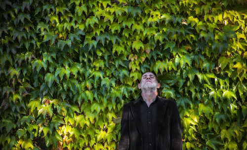 Portrait of adult man in black suit standing against green leaves