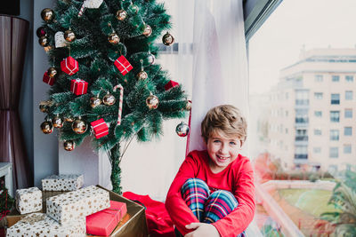 Portrait of boy sitting by christmas tree at home