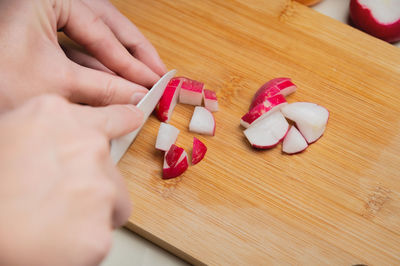 Close-up female hands of a young girl cut a fresh radish with a kitchen knife. preparing vegetable