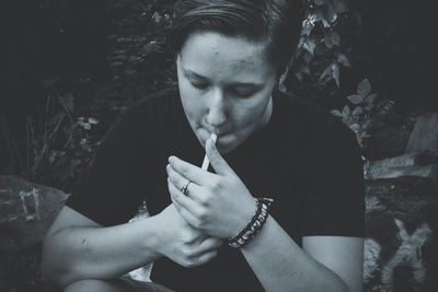 Woman smoking cigarette while sitting at forest