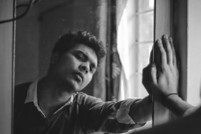 Portrait of young man looking through window at home