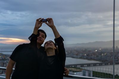 Rear view of friends standing against sky during sunset