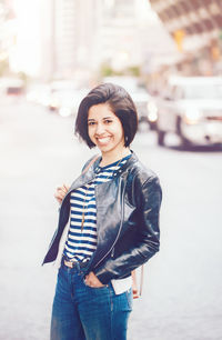 Portrait of smiling young woman standing on road in city