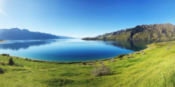 Scenic view of lake and mountains against clear blue sky