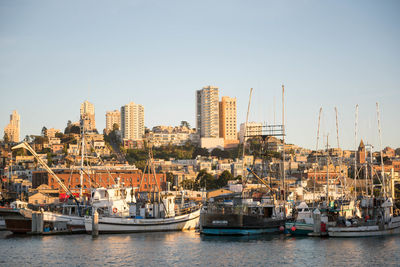 Sailboats moored on river by buildings in city against clear sky