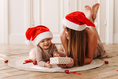 Happy family, cute mom and baby little daughter in santa hats celebrate christmas together at home