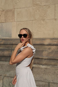 Young woman wearing sunglasses standing against wall