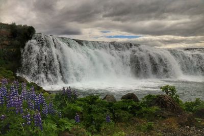 Scenic view of waterfall against cloudy sky