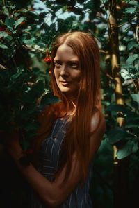 Portrait of beautiful young woman standing against trees