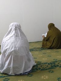 Rear view of woman reading books while sitting at temple