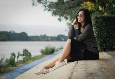 Portrait of young woman sitting against lake