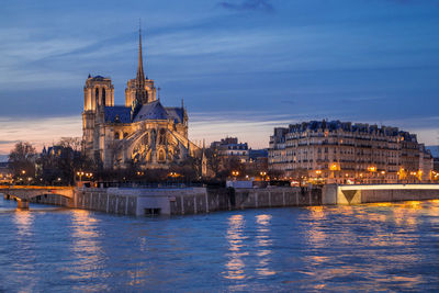 Illuminated notre dame cathedral and buildings in city against sky